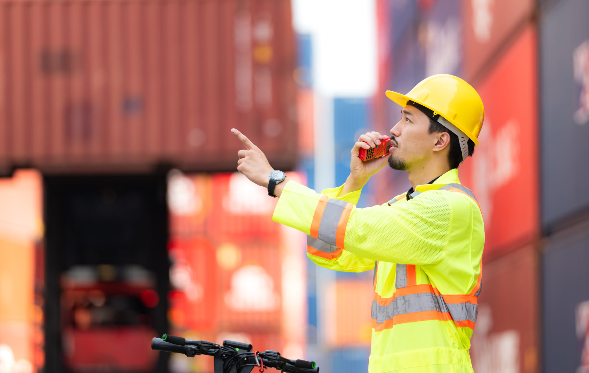 Portrait of a warehouse worker speaking on a walkie talkie with a coworker in an empty container warehouse while driving a scooter to inspect work